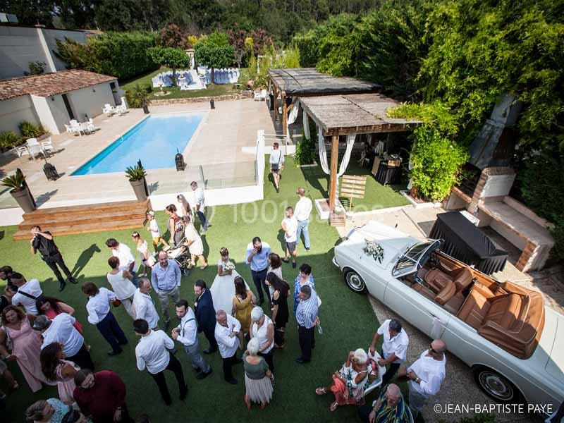 Vue aérienne d'une réception en plein air avec des invités, une piscine, une voiture ancienne et un espace aménagé.