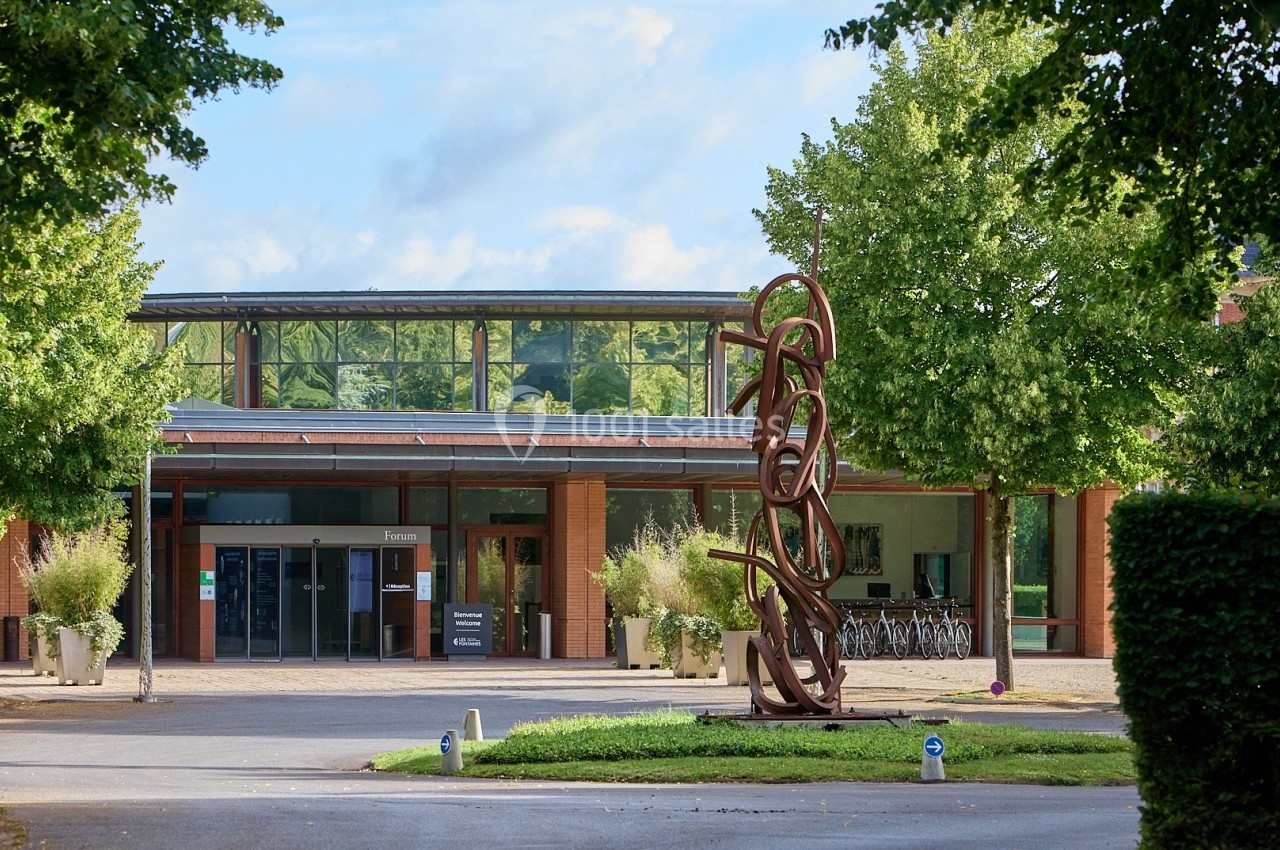 Entrée d'un bâtiment moderne avec une sculpture en métal devant et des arbres environnants.