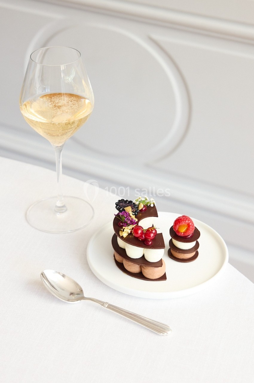 Dessert raffiné à base de chocolat et fruits rouges, servi sur une assiette blanche avec une coupe de vin blanc.
