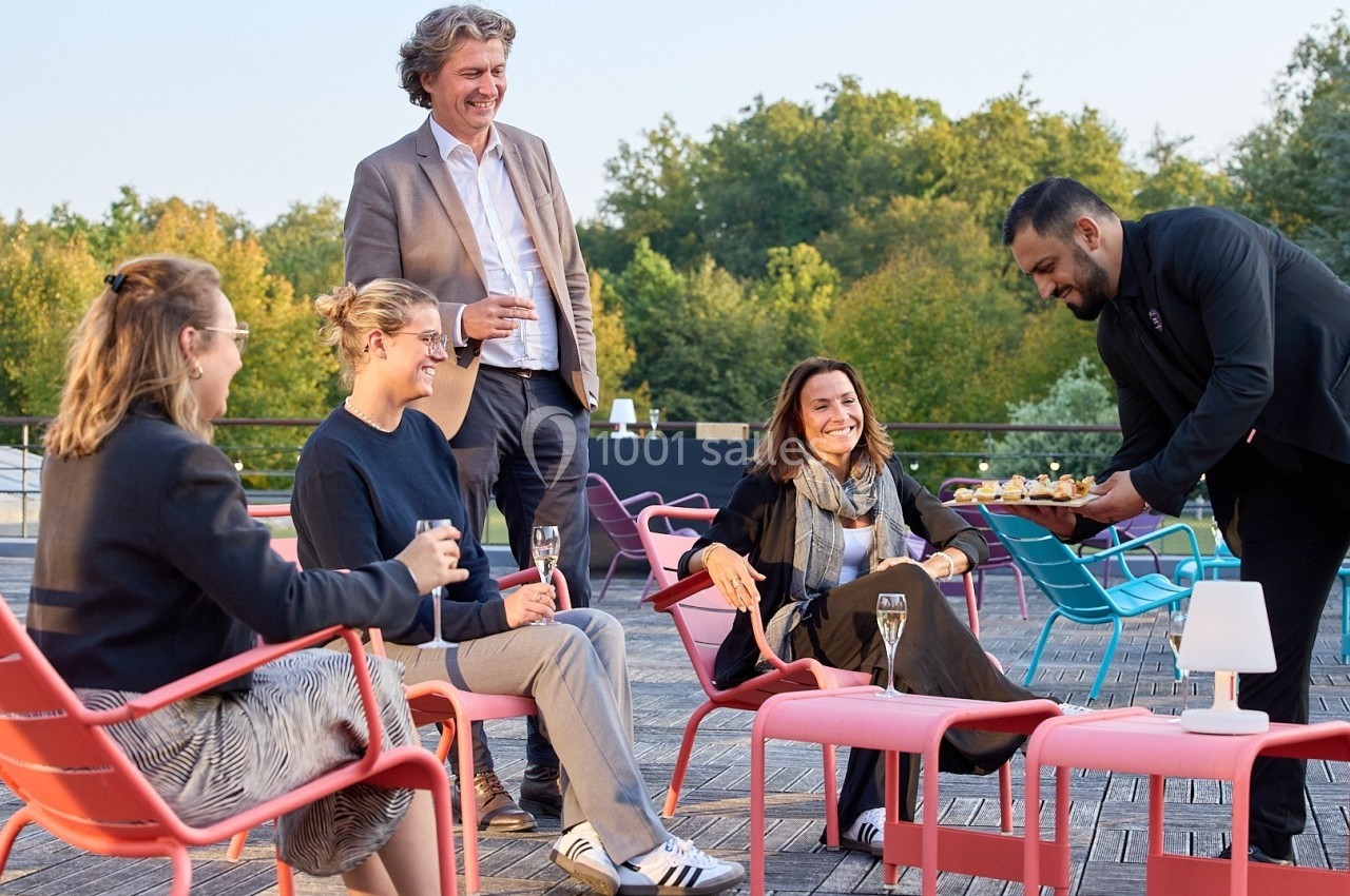 Un serveur propose des amuse-bouches à un groupe de personnes assises en extérieur sur une terrasse.