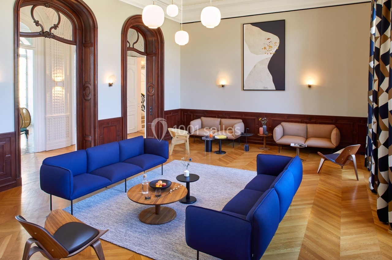 Salon élégant avec parquet en chevrons, canapés bleus et beiges, tables basses et éclairage moderne.