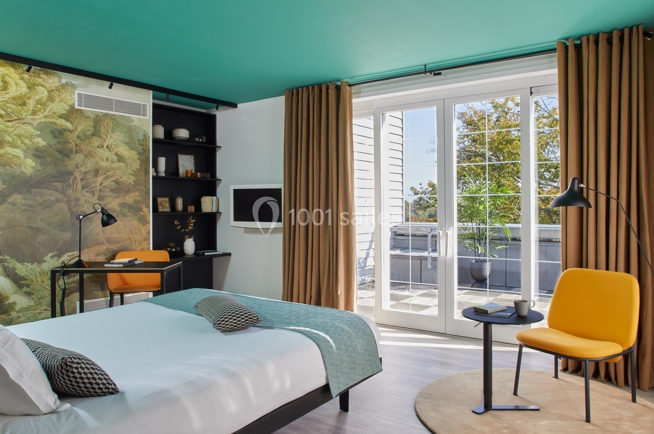 Chambre lumineuse avec lit, bureau, fauteuil jaune, mur décoré et grande baie vitrée donnant sur une terrasse.