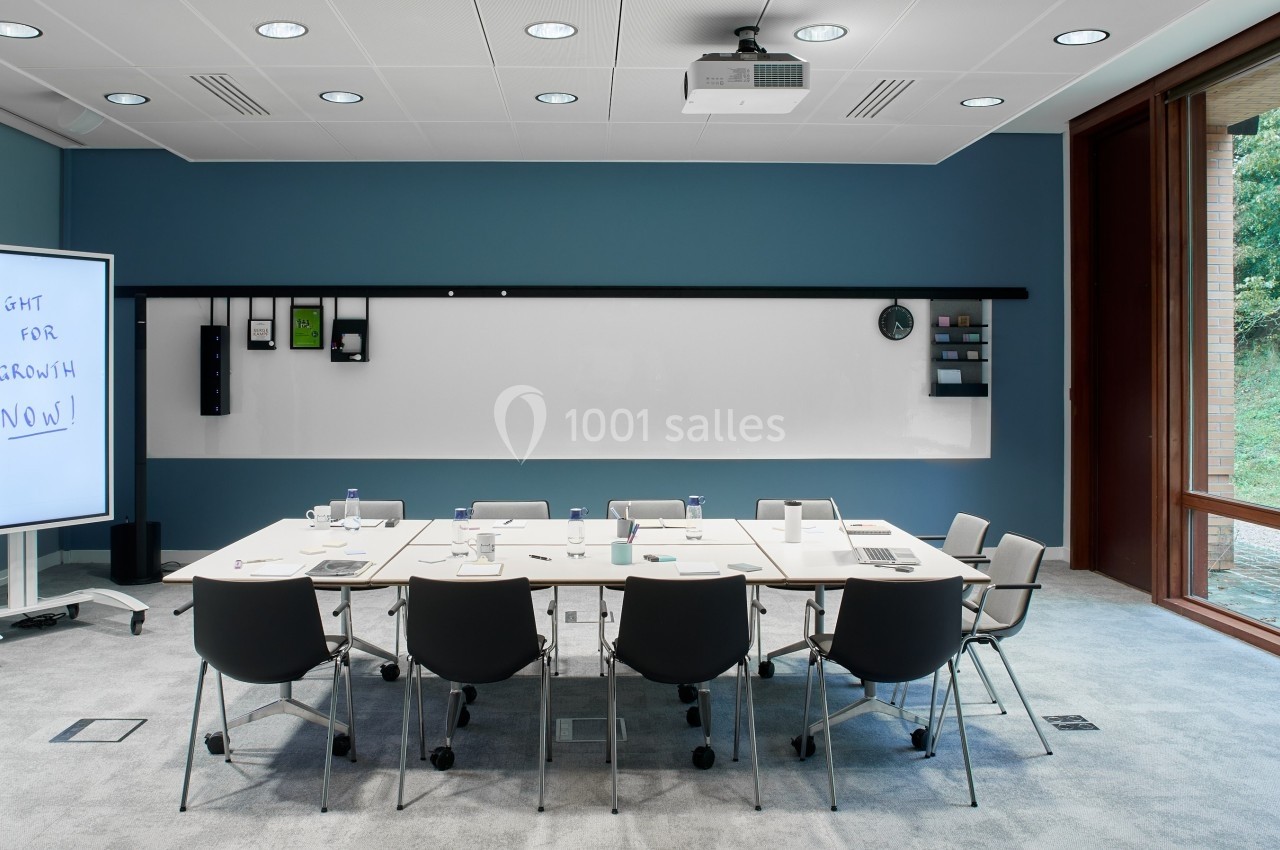 Salle de réunion moderne avec table, chaises, tableau blanc, écran interactif et vue sur un espace vert extérieur.