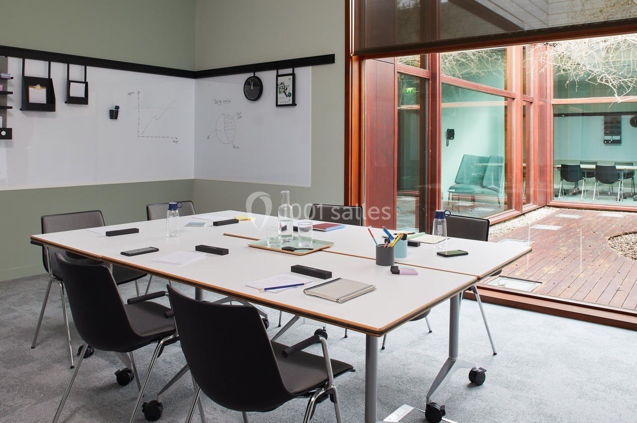 Salle de réunion moderne avec table, chaises, tableau blanc et vue sur un patio vitré.