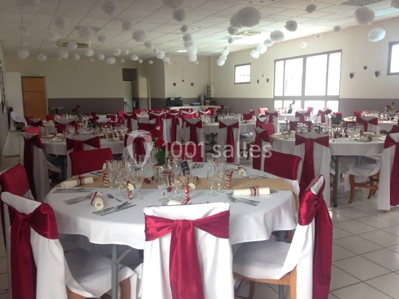 Salle de réception décorée avec des nappes blanches, des chaises ornées de nœuds rouges et des tables dressées pour un…