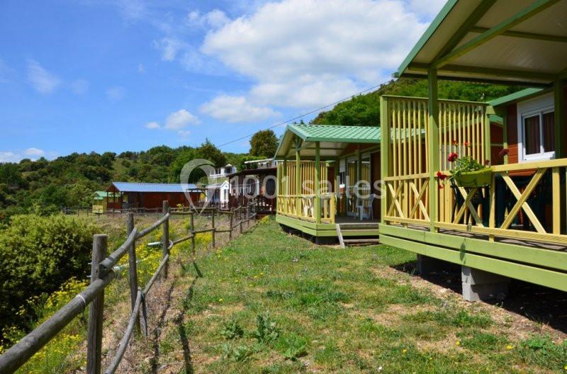 Chalets en bois avec terrasses, situés sur une colline verdoyante sous un ciel partiellement nuageux.