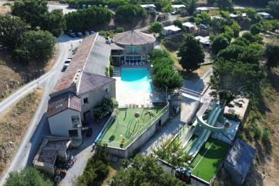 Vue aérienne d'un complexe avec piscine, toboggan aquatique, mini-golf et espaces ombragés entourés de végétation.