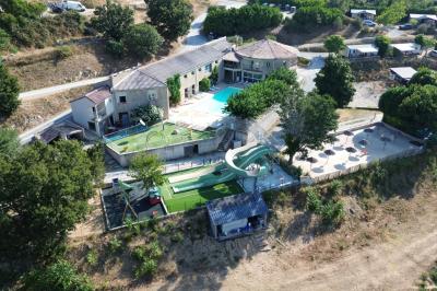 Vue aérienne d'un complexe avec piscine, toboggan aquatique, mini-golf et espaces ombragés entourés de végétation.