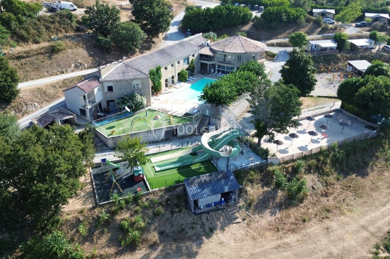 Vue aérienne d'un complexe avec piscine, toboggan aquatique, mini-golf et espaces ombragés entourés de végétation.