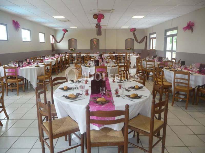 Salle de réception décorée avec des nappes blanches et des accents roses, tables dressées pour un repas.