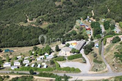Vue aérienne d'un complexe avec piscine, toboggan aquatique, mini-golf et espaces ombragés entourés de végétation.