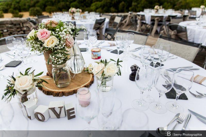 Table décorée pour un événement avec fleurs, rondin de bois, verres et lettres formant le mot ’LOVE’.