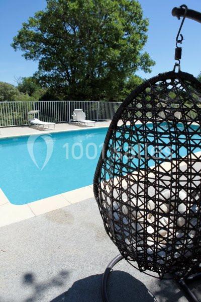 Fauteuil suspendu en rotin près d'une piscine extérieure entourée de chaises longues et d'arbres.