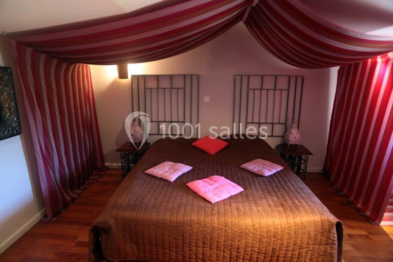 Lit double avec couvre-lit marron, coussins roses et rideaux rayés rouges et blancs formant un baldaquin.