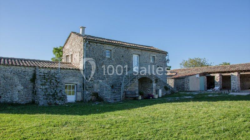 Maison en pierre traditionnelle avec escalier extérieur, entourée de pelouses et bâtiments annexes sous un ciel dégagé.
