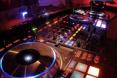 Table de mixage DJ éclairée avec des boutons, des curseurs et des platines lumineuses dans une ambiance sombre.