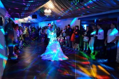 Un couple danse sous des lumières colorées lors d'une réception, entouré d'invités debout.
