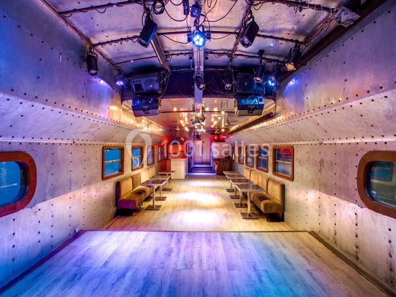 Intérieur d'un wagon aménagé avec des banquettes, un éclairage coloré et un espace central dégagé.