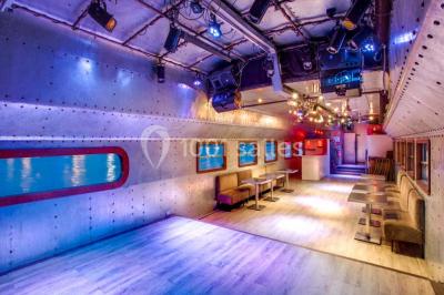 Salle avec tables et chaises en bois sur une péniche, offrant une vue sur un pont et une rivière en arrière-plan.