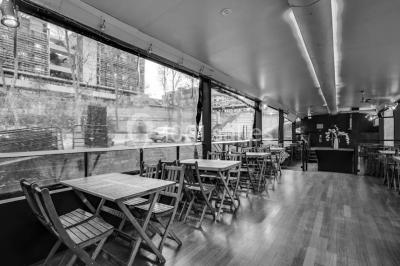 Salle avec tables et chaises en bois sur une péniche, offrant une vue sur un pont et une rivière en arrière-plan.
