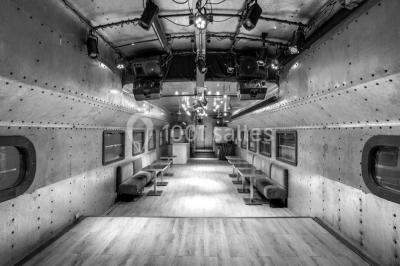 Salle avec tables et chaises en bois sur une péniche, offrant une vue sur un pont et une rivière en arrière-plan.