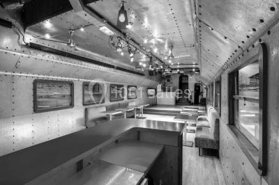 Salle avec tables et chaises en bois sur une péniche, offrant une vue sur un pont et une rivière en arrière-plan.