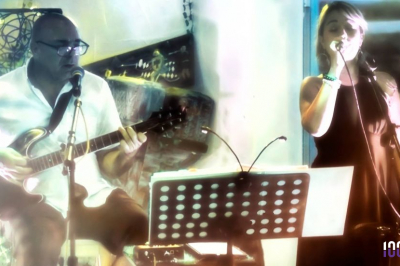 Un homme jouant de la guitare et une femme souriante posent devant des micros à bord d'un bateau.