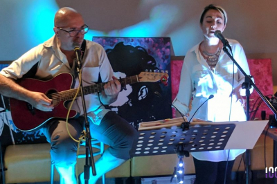 Un homme jouant de la guitare et une femme souriante posent devant des micros à bord d'un bateau.