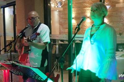Un homme jouant de la guitare et une femme souriante posent devant des micros à bord d'un bateau.