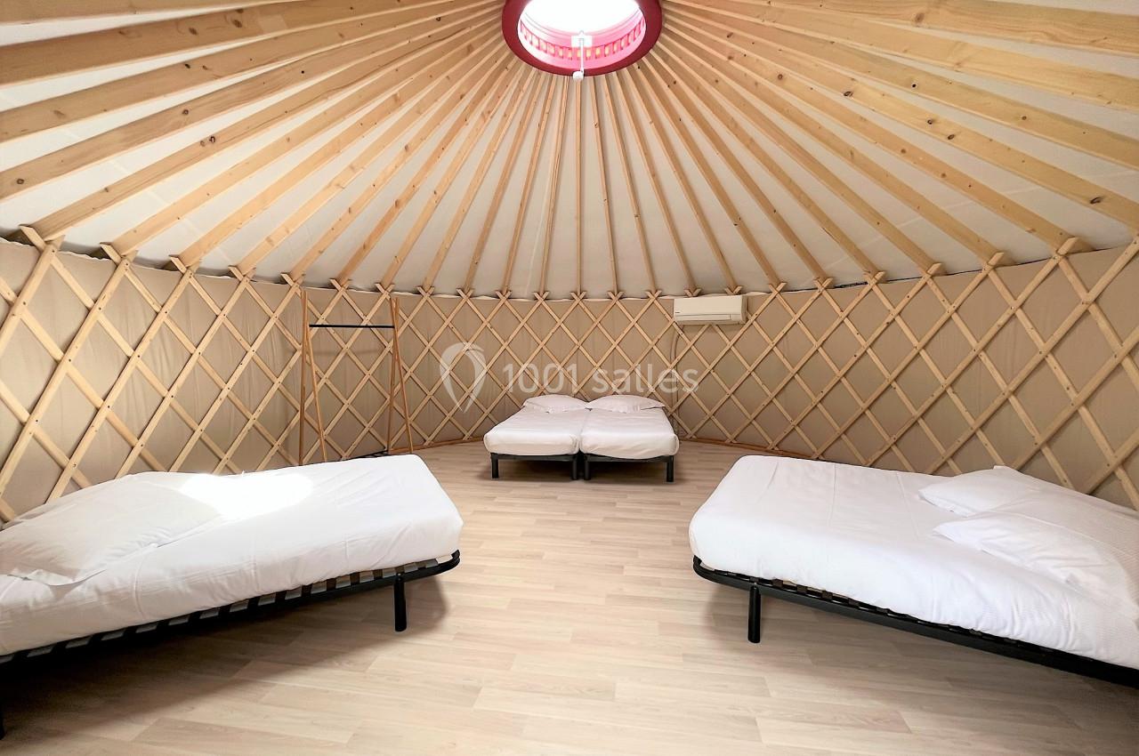 Intérieur d'une yourte avec trois lits simples, sol en bois clair et structure en bois visible.