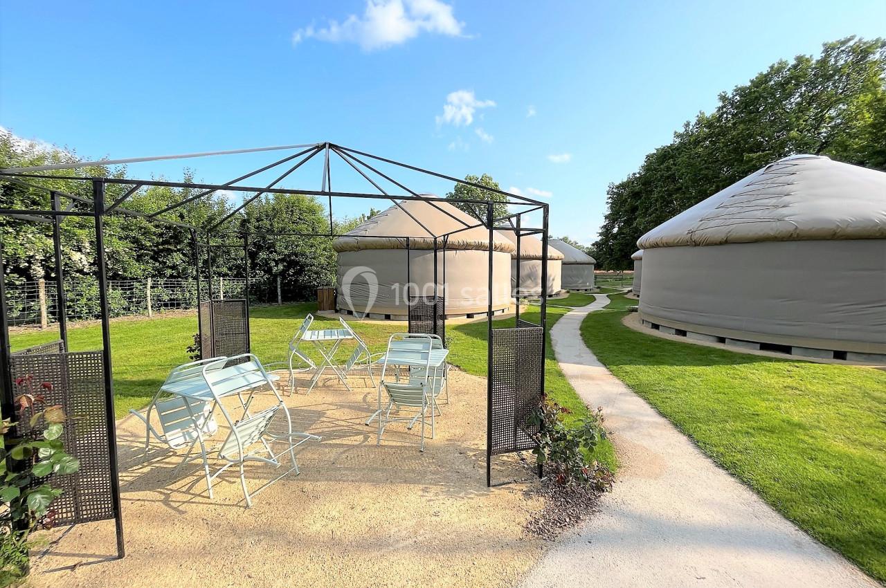 Espace extérieur avec pergola, chaises et tables, entouré de yourtes sur une pelouse bien entretenue.