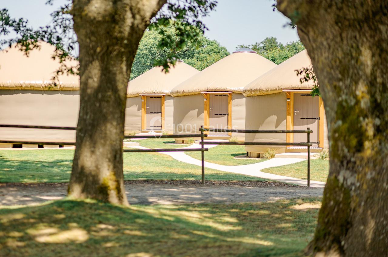 Alignement de plusieurs yourtes beige clair dans un espace verdoyant, entourées d'arbres et de chemins sinueux.
