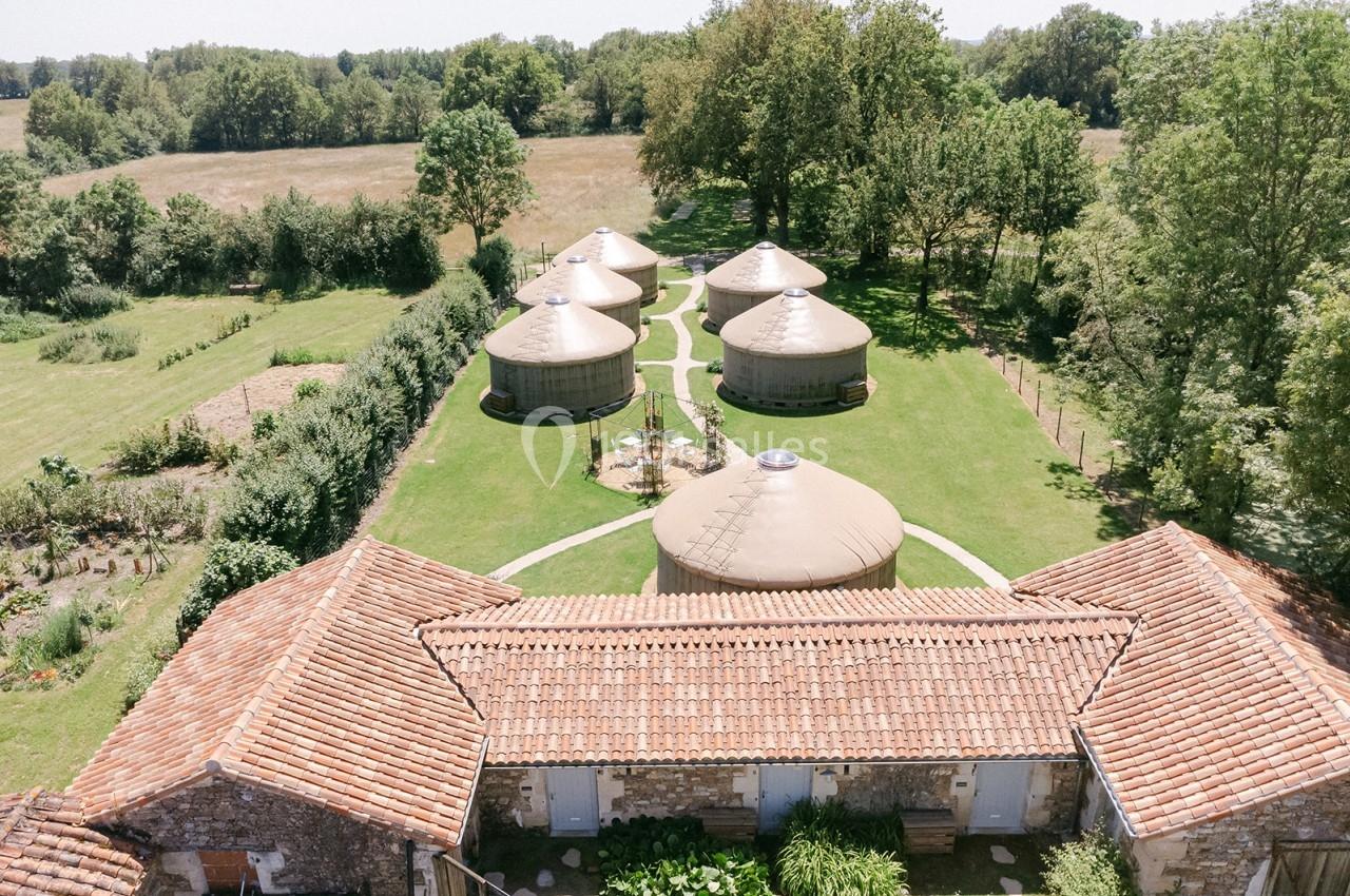 Vue aérienne de plusieurs yourtes entourées de verdure, avec des bâtiments en pierre au premier plan.