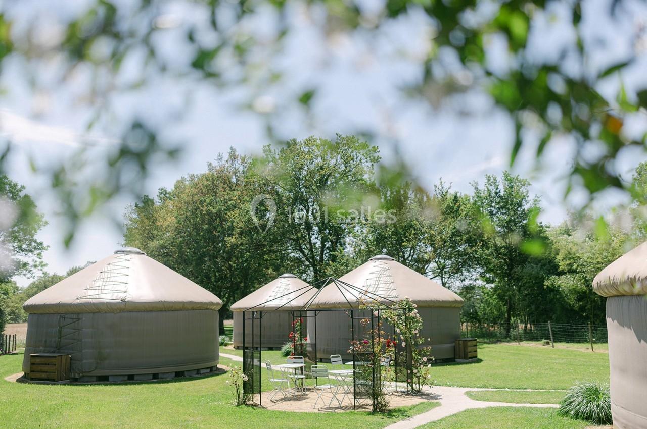 Trois yourtes beige clair entourées de verdure, avec un salon de jardin sous une pergola au premier plan.