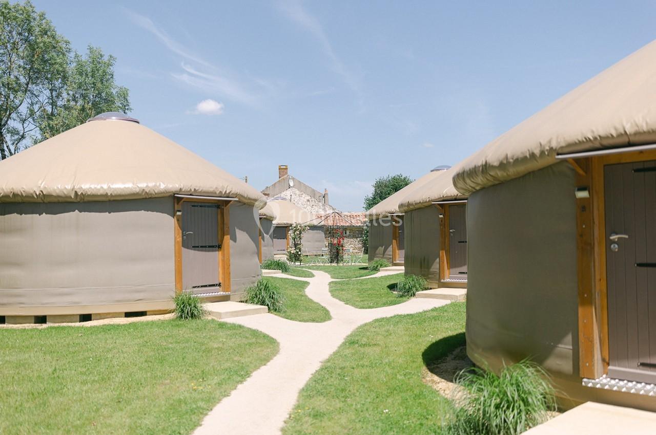 Plusieurs yourtes modernes disposées sur une pelouse avec des chemins en gravier sous un ciel bleu.