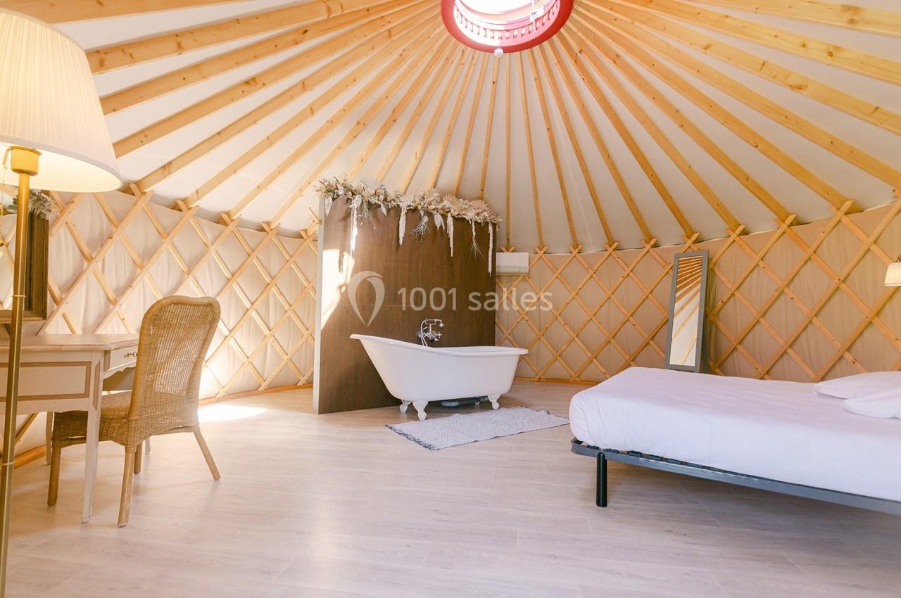 Intérieur d'une yourte lumineuse avec baignoire, lit, bureau et décoration en bois clair.