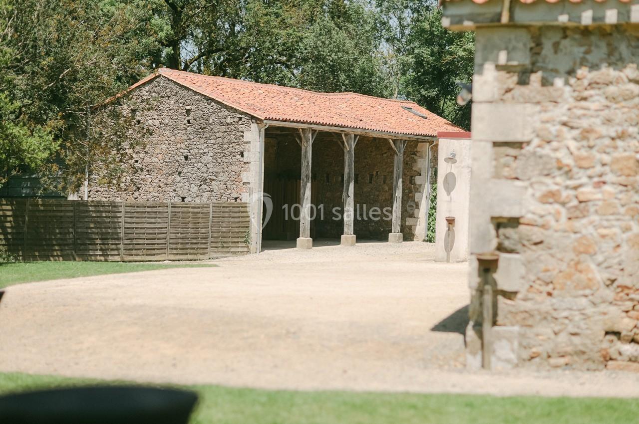 Bâtiment en pierre avec toit en tuiles rouges, entouré d'arbres et d'une cour en gravier.