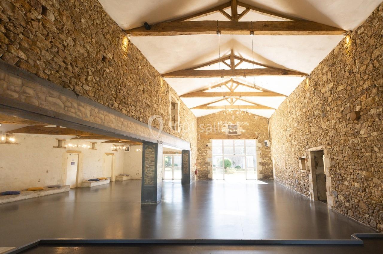 Intérieur d'une grande salle avec murs en pierre apparente, poutres en bois au plafond et sol lisse.