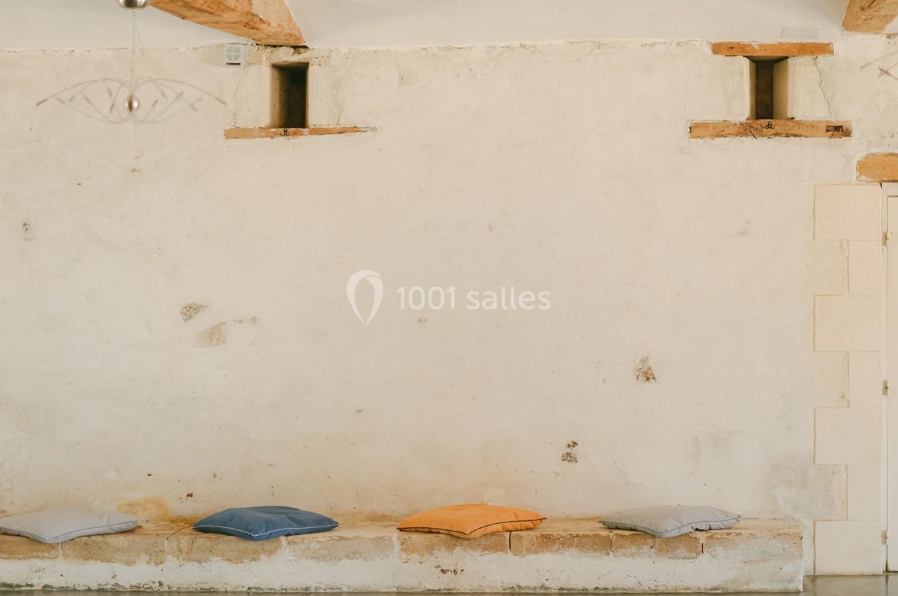 Coussins colorés disposés sur un banc en pierre contre un mur beige dans une pièce lumineuse.