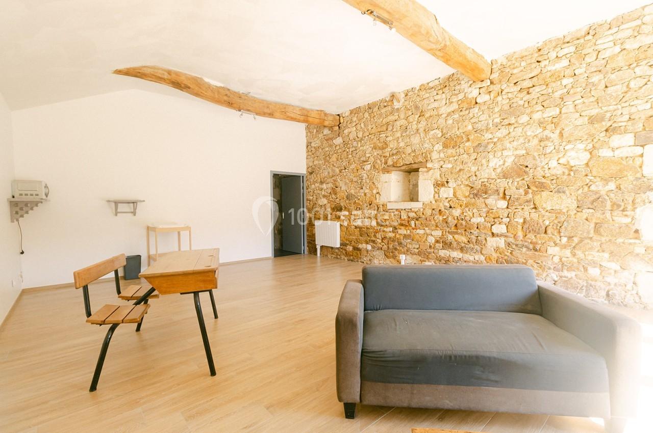 Salle lumineuse avec murs en pierre, poutres apparentes, parquet clair, canapé gris et mobilier en bois minimaliste.