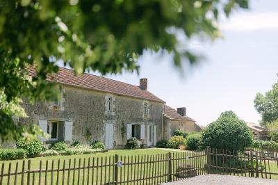 Chemin de gravier menant à une maison en pierre avec toit en tuiles, entourée de verdure et d'une clôture en bois.