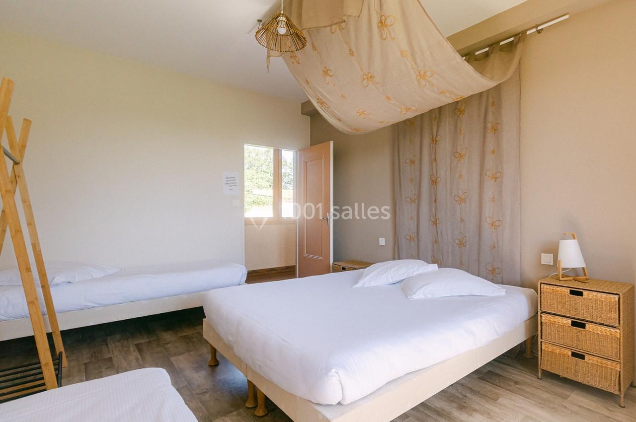 Chambre lumineuse avec trois lits simples, sol en parquet, mobilier en bois clair et rideaux beige décoratifs.