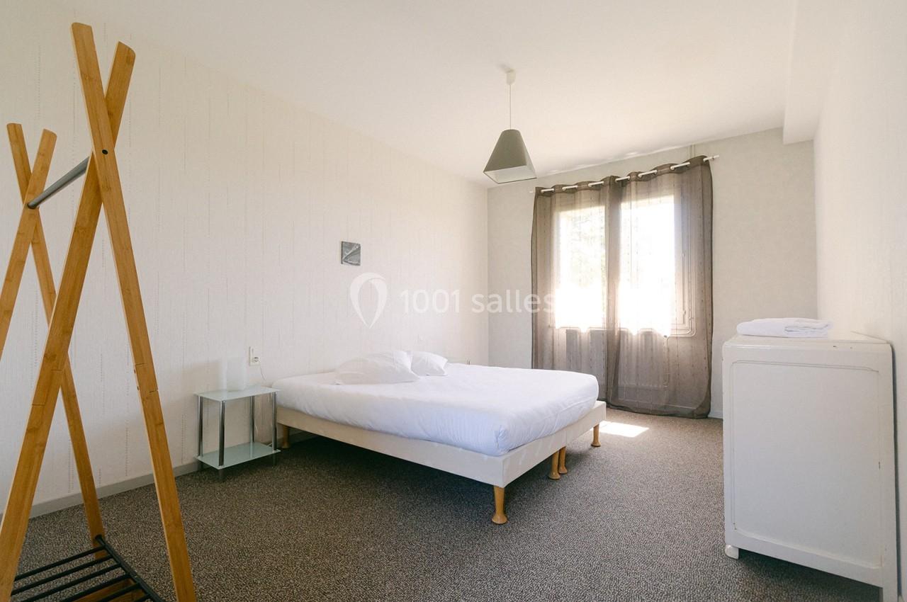 Chambre lumineuse avec un lit double, un portant en bois, une table de chevet et une fenêtre avec rideaux.