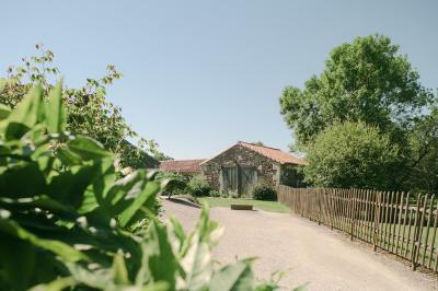 Chemin de gravier menant à une maison en pierre avec toit en tuiles, entourée de verdure et d'une clôture en bois.
