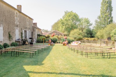 Chemin de gravier menant à une maison en pierre avec toit en tuiles, entourée de verdure et d'une clôture en bois.