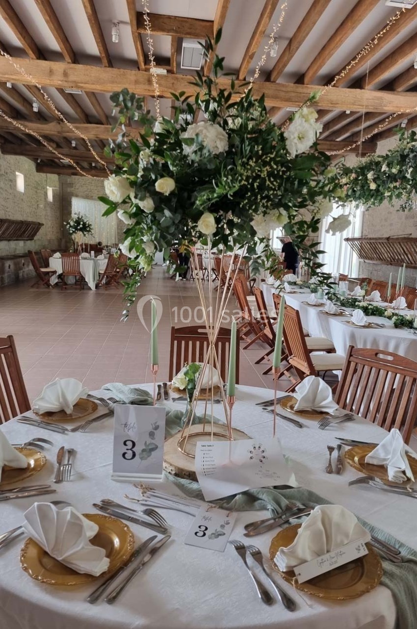 Salle de réception décorée avec des tables élégantes, nappes blanches, centres de table fleuris et chaises en bois.