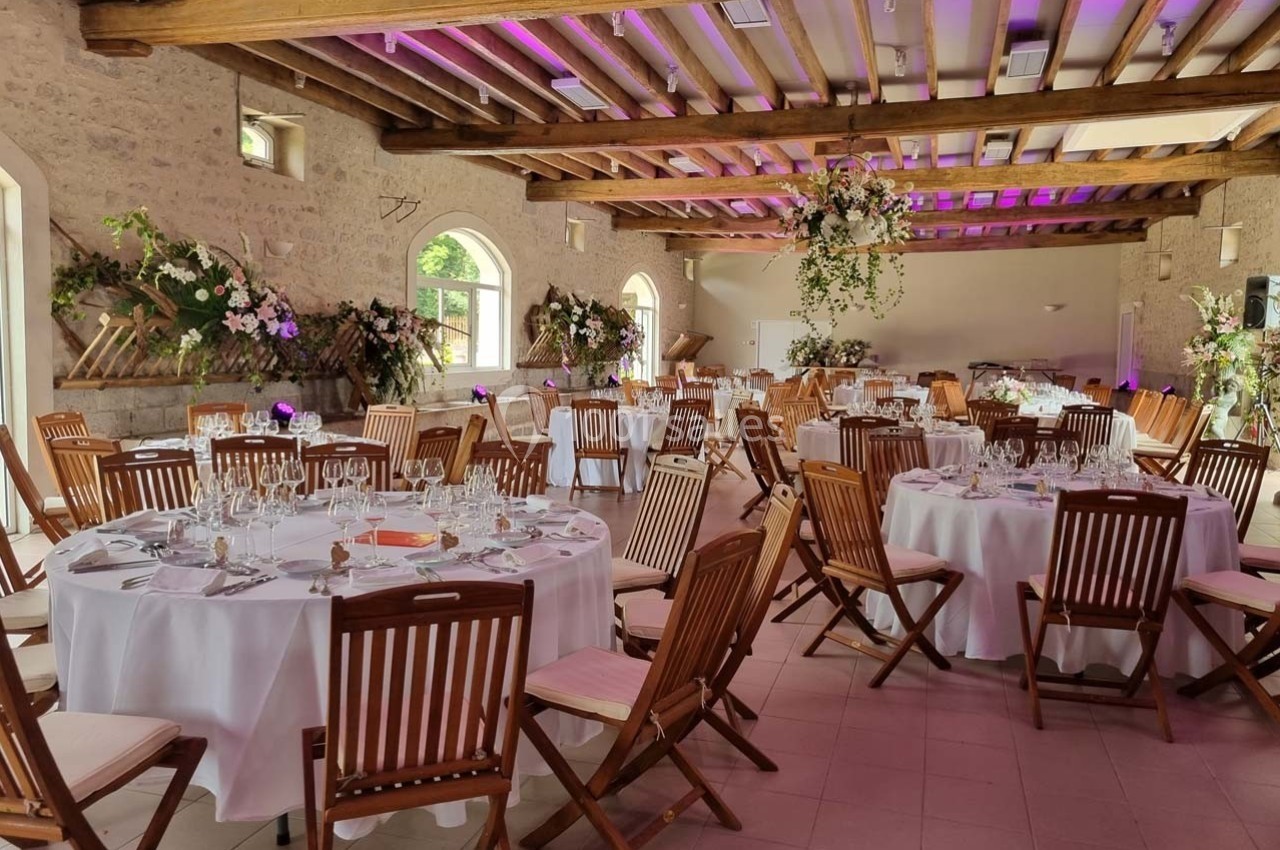 Salle de réception décorée avec des tables rondes dressées, chaises en bois et arrangements floraux élégants.