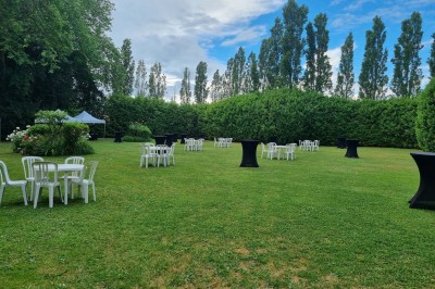 Chaises blanches disposées en rangées sur une pelouse, face à une petite scène décorée pour un événement en plein air.