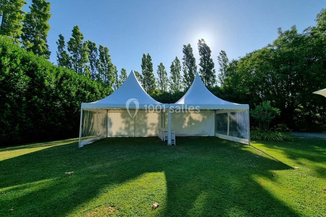 Deux tentes blanches avec toits pointus installées sur une pelouse entourée d'arbres sous un ciel dégagé.