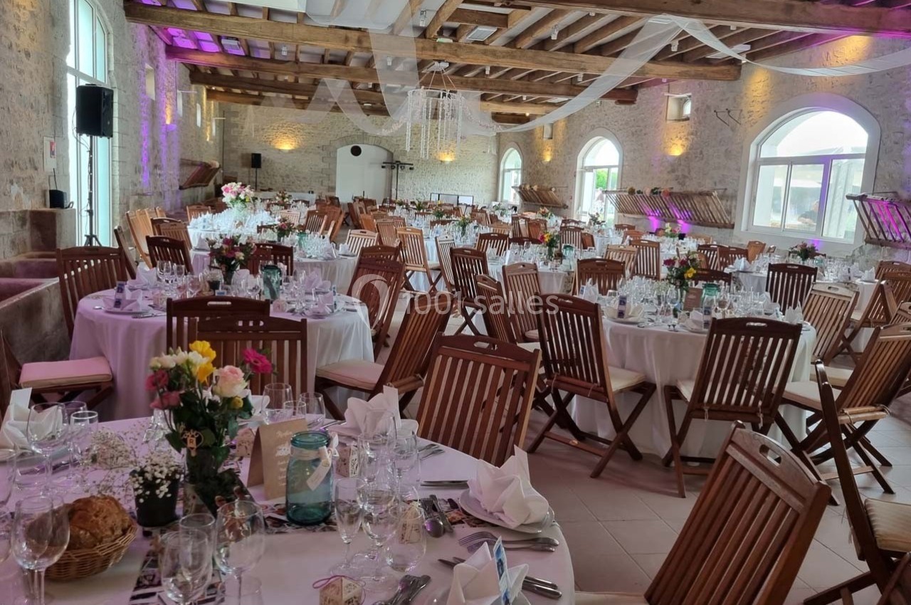 Salle de réception décorée avec des tables rondes dressées, chaises en bois et éclairage tamisé.